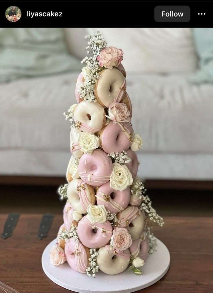 Tall tower of pink and white glazed donuts decorated with roses and baby's breath.