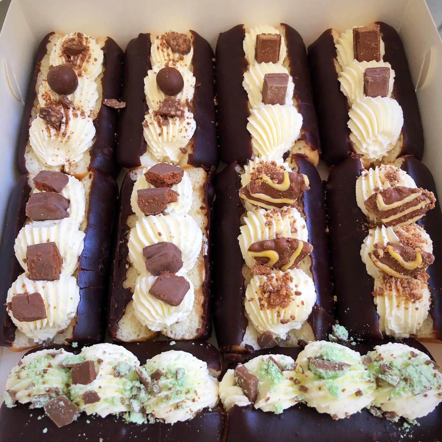 Chocolate-dipped eclairs filled with whipped cream and topped with assorted chocolate candy pieces.