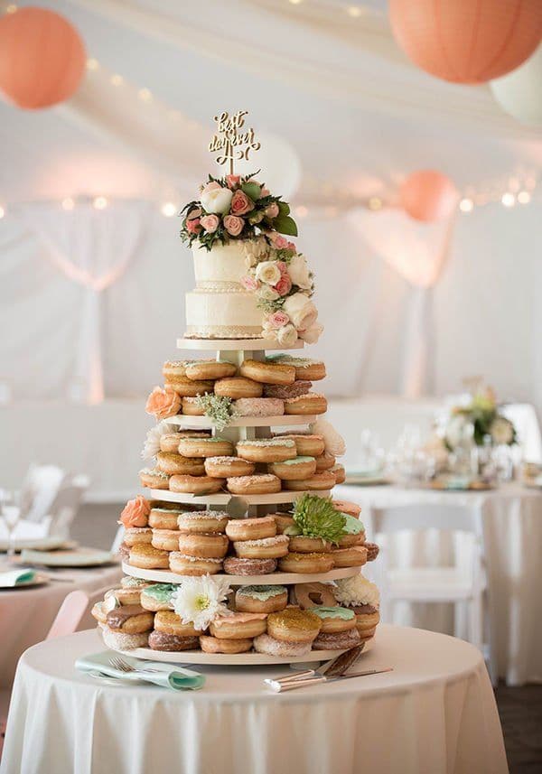 Tiered wedding dessert stand with a floral white cake and layers of assorted glazed donuts.