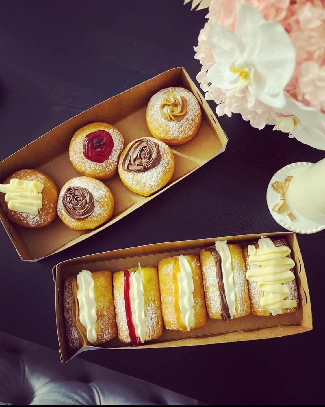 Two boxes of assorted round and rectangular donuts topped with colorful cream, jam, and chocolate.