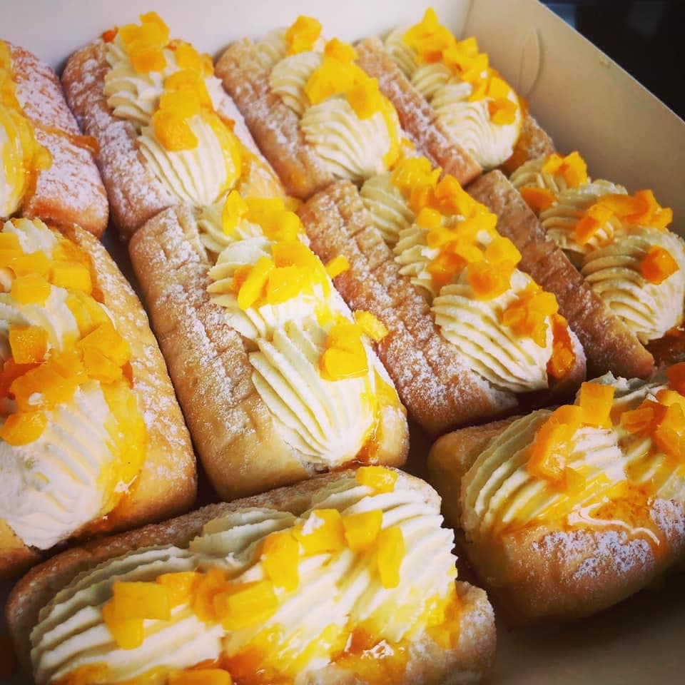 Rectangular powdered donuts filled with piped white cream and topped with diced yellow fruit pieces.